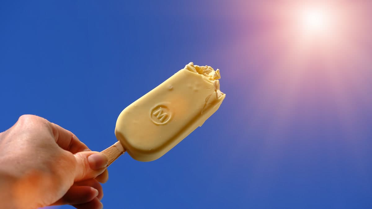 Elde tutulan bir Magnum dondurma çubuğu, üzerindeki kabartma 'M' logosuyla gökyüzüne doğru kaldırılmış
