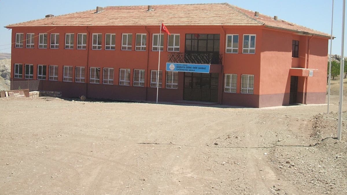 Türk bayrağı direği önünde iki katlı ilköğretim okulu binası ve geniş okul bahçesi (temsilî görsel)