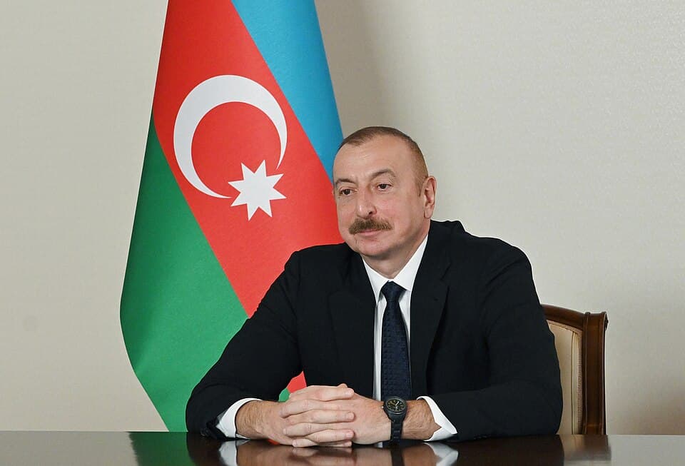 Azerbaycan Cumhurbaşkanı İlham Aliyev bir görüşme masasında, arkasında Azerbaycan bayrağı